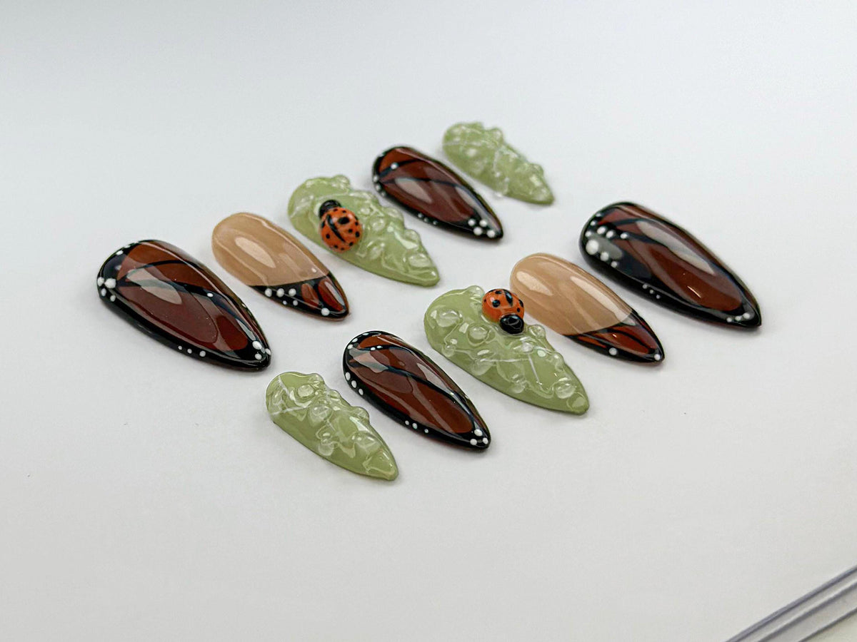 Brown and Black Wing-Inspired Nails With Green Dewdrops and Ladybugs