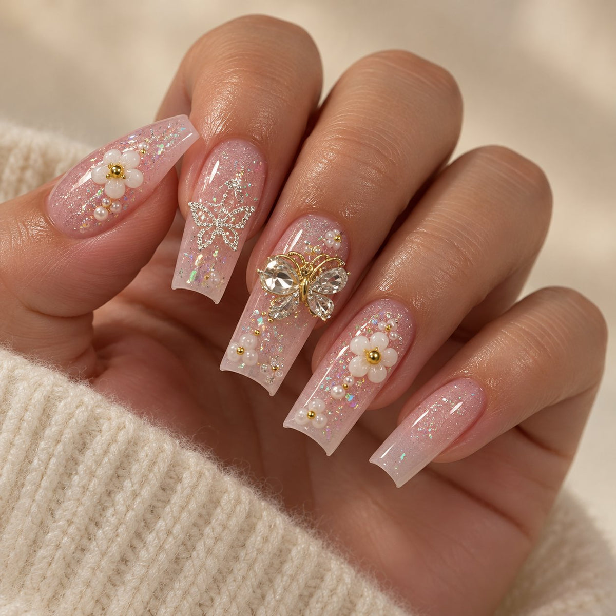 Nude Pink Floral Nails With Rhinestones, Gold Charms, and Glitter worn on hand