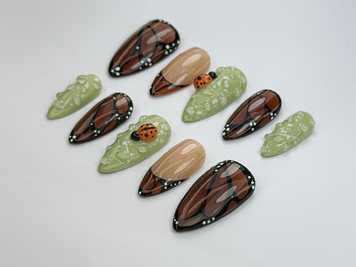 Brown and Black Wing-Inspired Nails With Green Dewdrops and Ladybugs