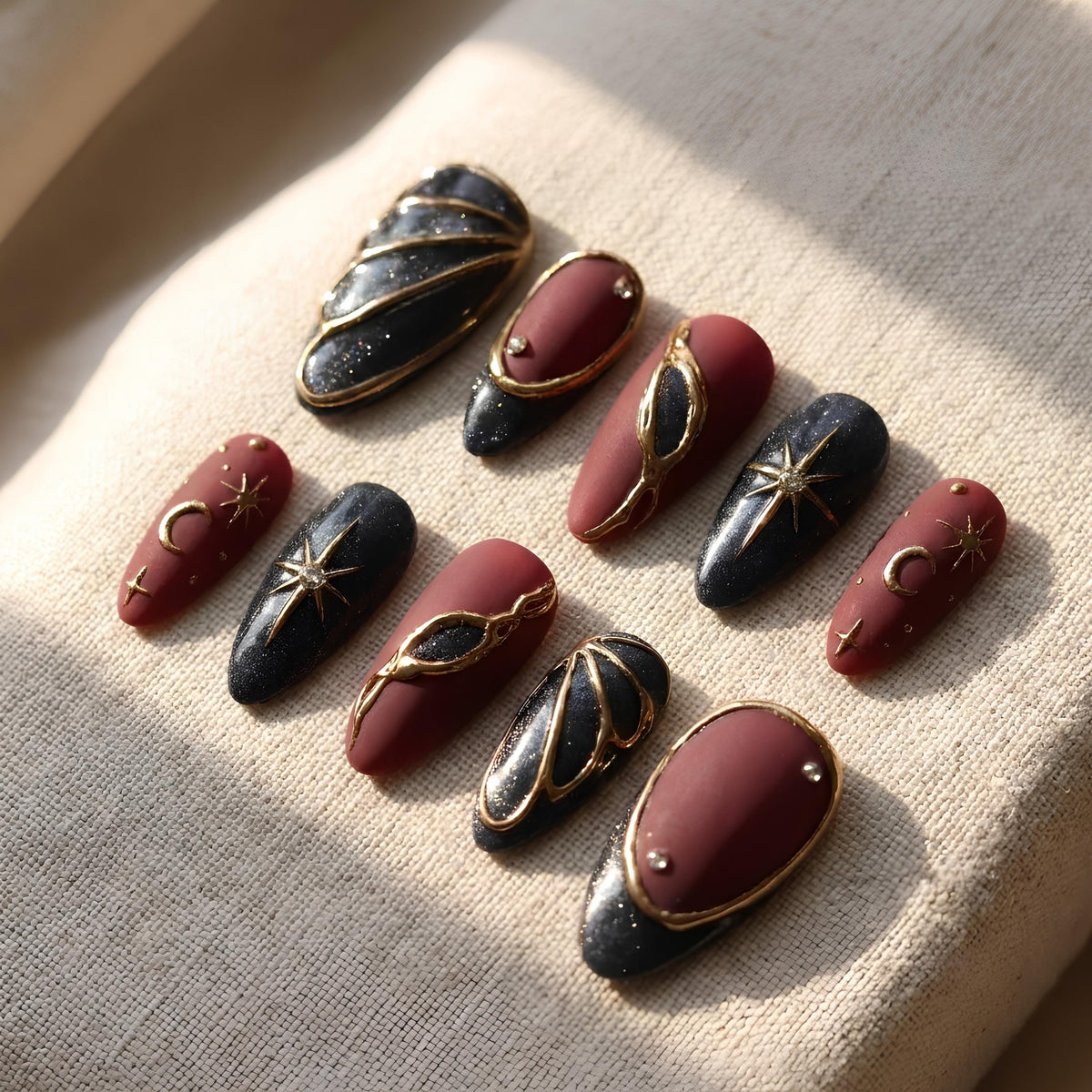 Burgundy and Black Celestial Nails with Gold Stars, Moons, and Rhinestone Accents