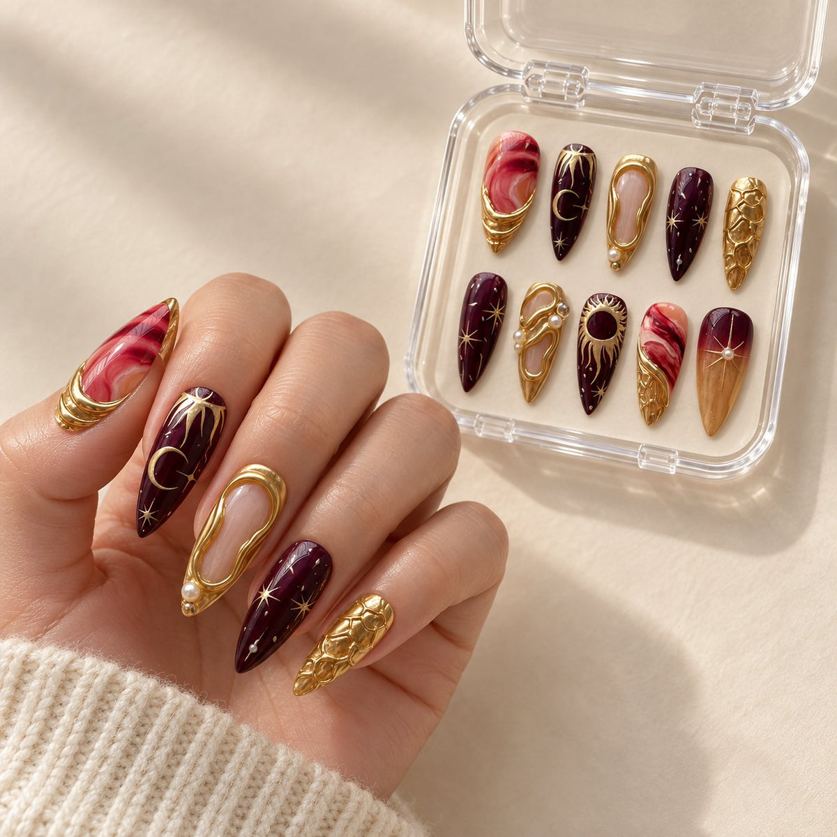 Burgundy and Gold 3D Sculptural Press-On Nails with Marble Swirls worn on hand with acrylic storage box