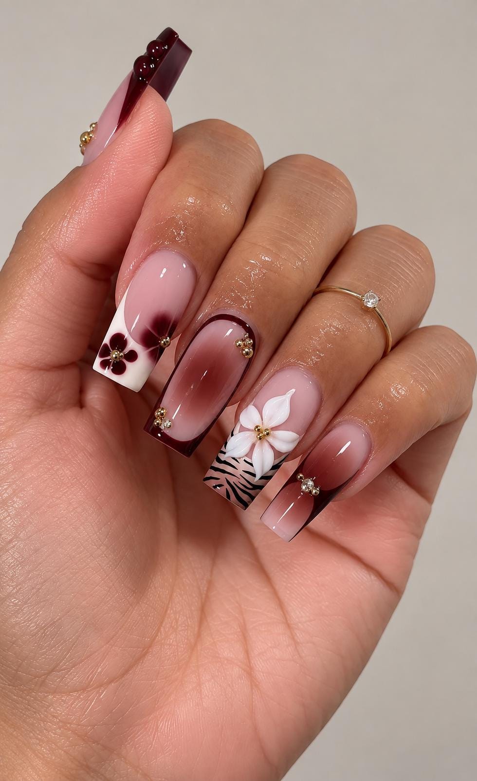 Burgundy French Tip Nails With Floral Details, Zebra Print, and Gold Accents