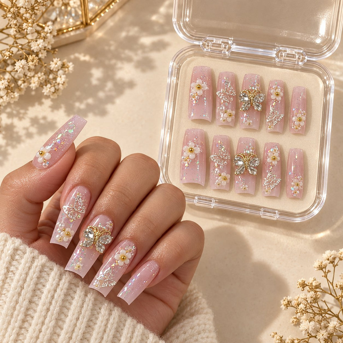 Nude Pink Floral Nails With Rhinestones, Gold Charms, and Glitter worn on hand with acrylic storage box