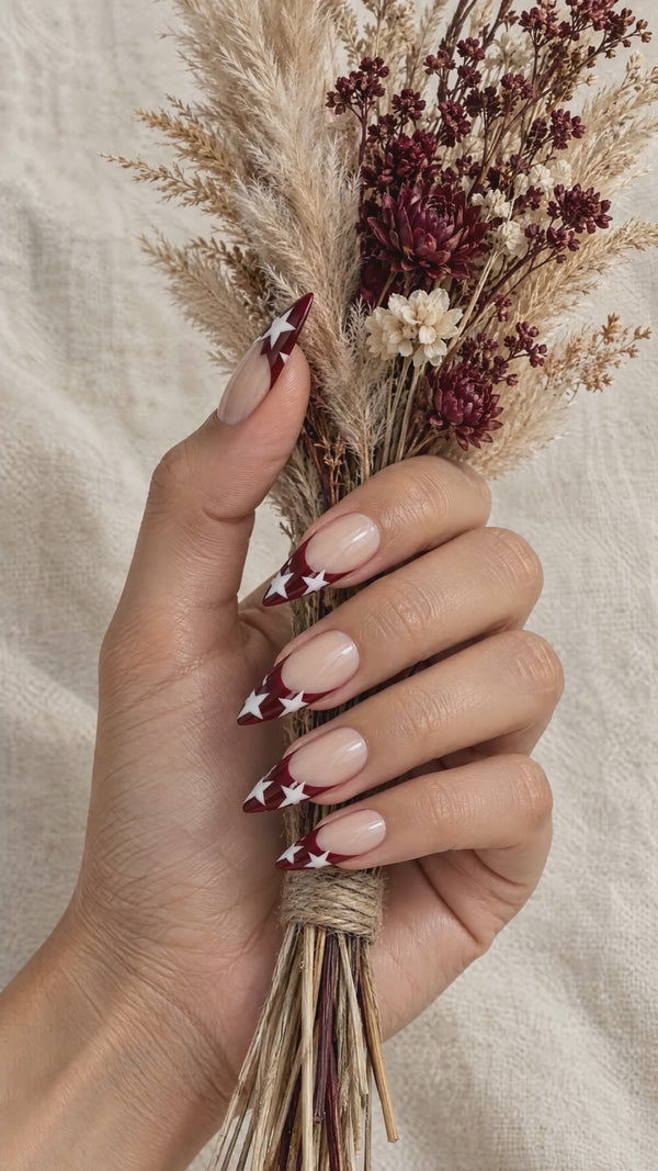 Burgundy star French tip press-on nails holding a dried flower bouquet